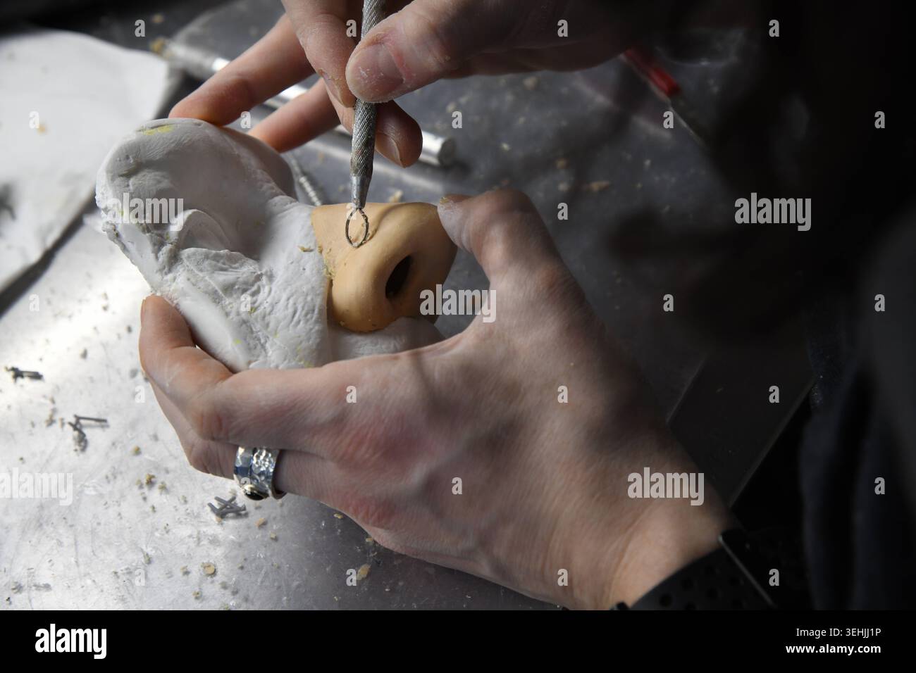 Ocularist using a small metal tool to sculpt a beige prosthetic nose ...