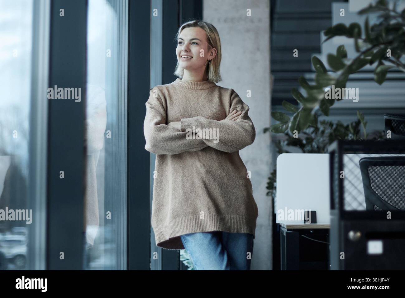 A woman stands in front of a window with her arms crossed Stock Photo ...