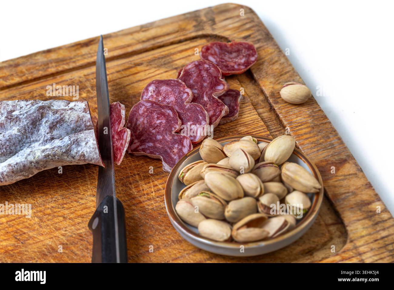 A wooden cutting board holds a knife, a piece of sliced salami, and a ...