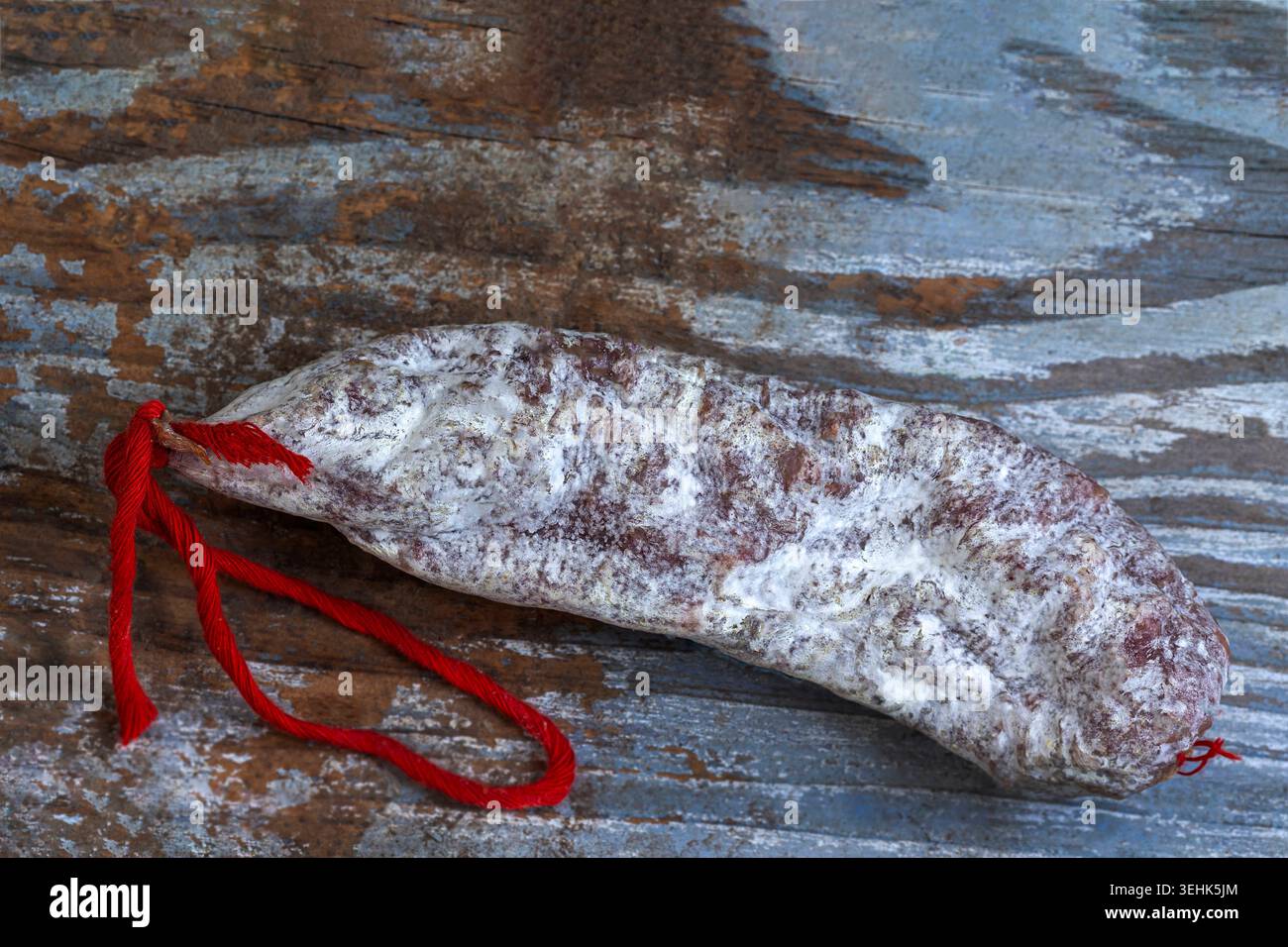 A cured salami with a white mold coating and a red string tie rests on ...