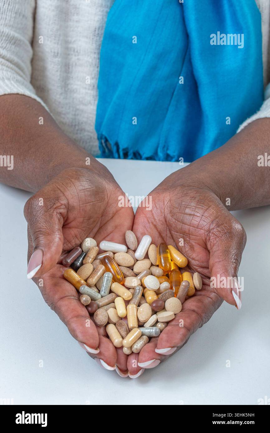 Two hands hold a variety of capsules and tablets. Medication handling ...