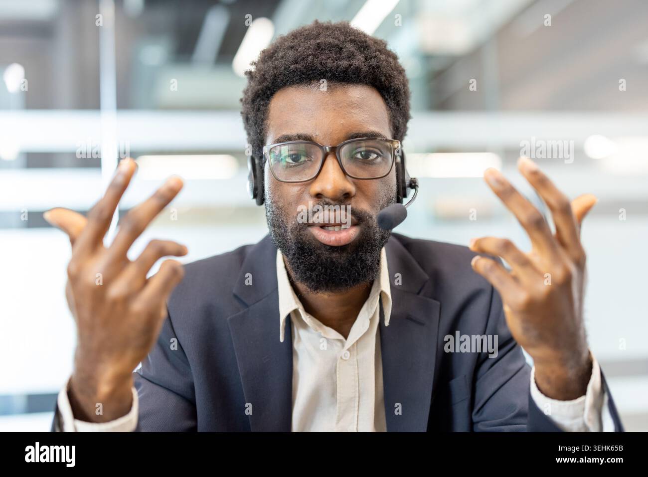 Confident customer service agent wearing a headset and glasses, communicating with clients, providing support, discussing solutions, and offering professional assistance in an office environment Stock Photo