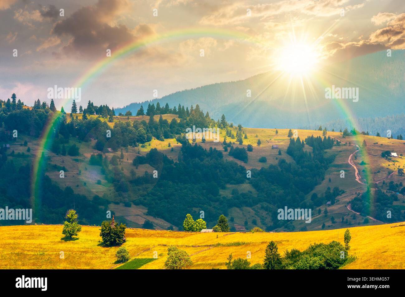 sunset over agricultural field on hillside in mountains near village. summer evening. green carpathian mountain landscape. narrow view. remote alpine Stock Photo