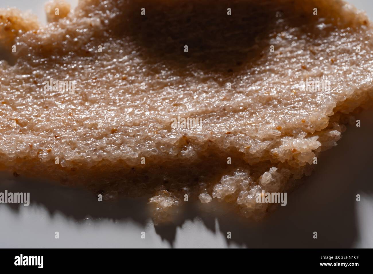 Macro close-up of a creamy body scrub smear with grainy exfoliating texture. Natural cosmetic product background showing thick paste, sugar crystals, Stock Photo