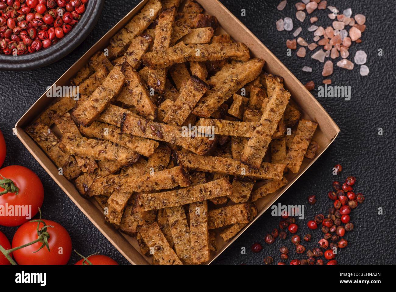 Food, Crispy homemade brown bread crackers or croutons with seeds and grains, salt, spices and herbs on a dark concrete background Stock Photo