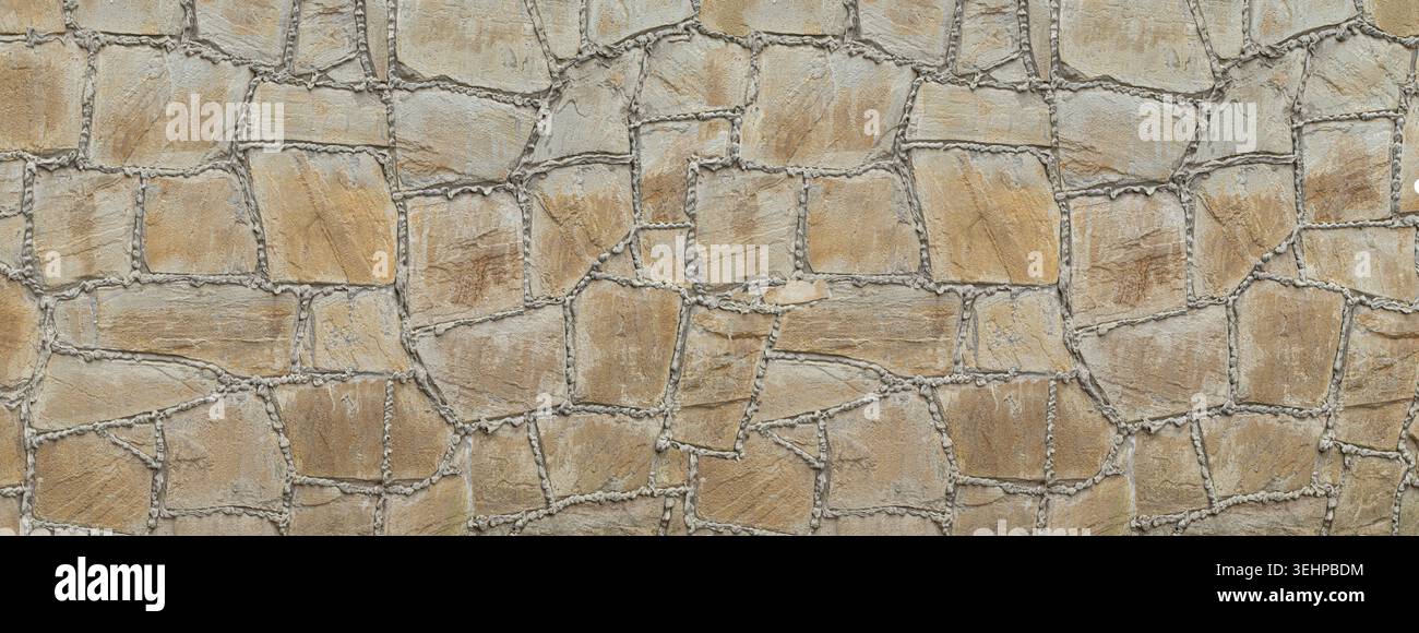Rough textured brown and gray stone masonry wall with irregular shapes and cement joints Stock Photo