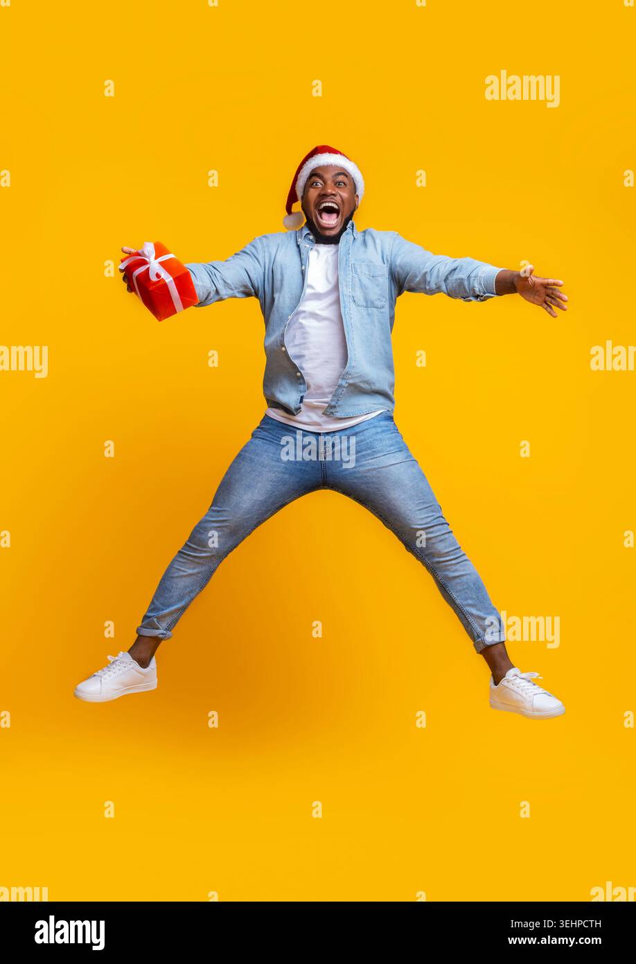 Overjoyed afro guy in santa hat jumping with gift box Stock Photo