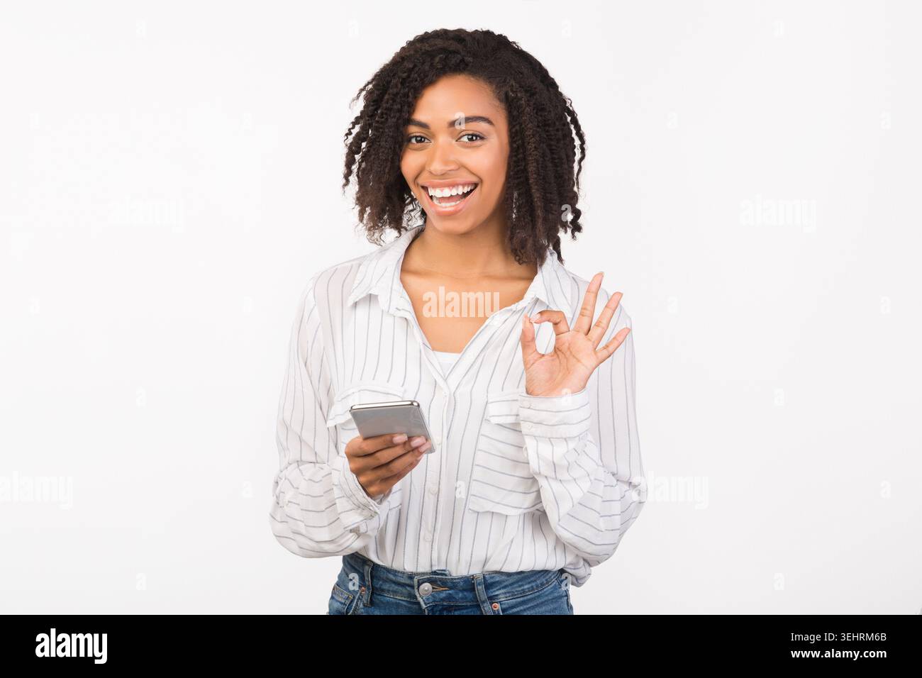 Portrait of smiling afro girl using phone showing ok gesture Stock Photo
