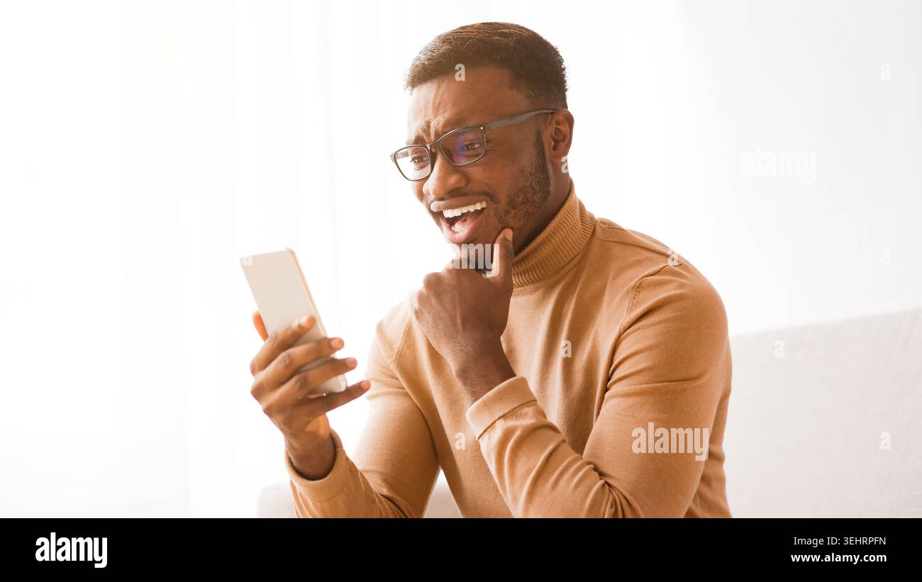 Cheerful man using phone chatting online sitting on sofa, panorama Stock Photo