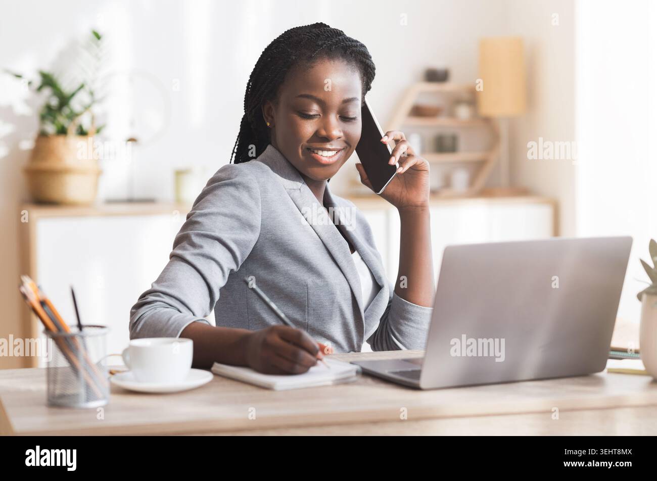 Afro Businesswoman Taking Notes While Having Phone Conversation In Modern Office Stock Photo