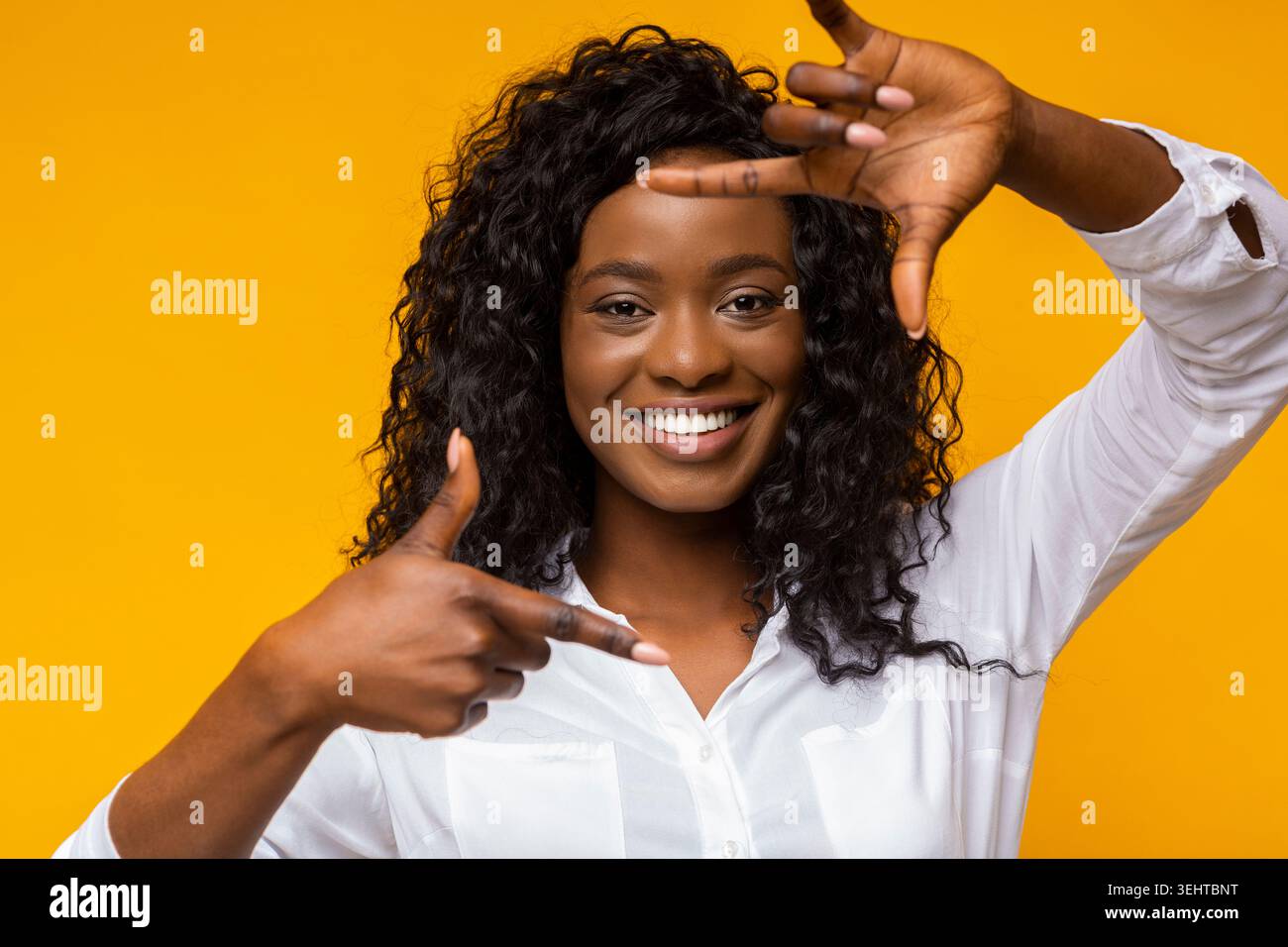 Smiling Woman Framing Her Face Against a Bright Yellow Background in a Cheerful Indoor Setting Stock Photo