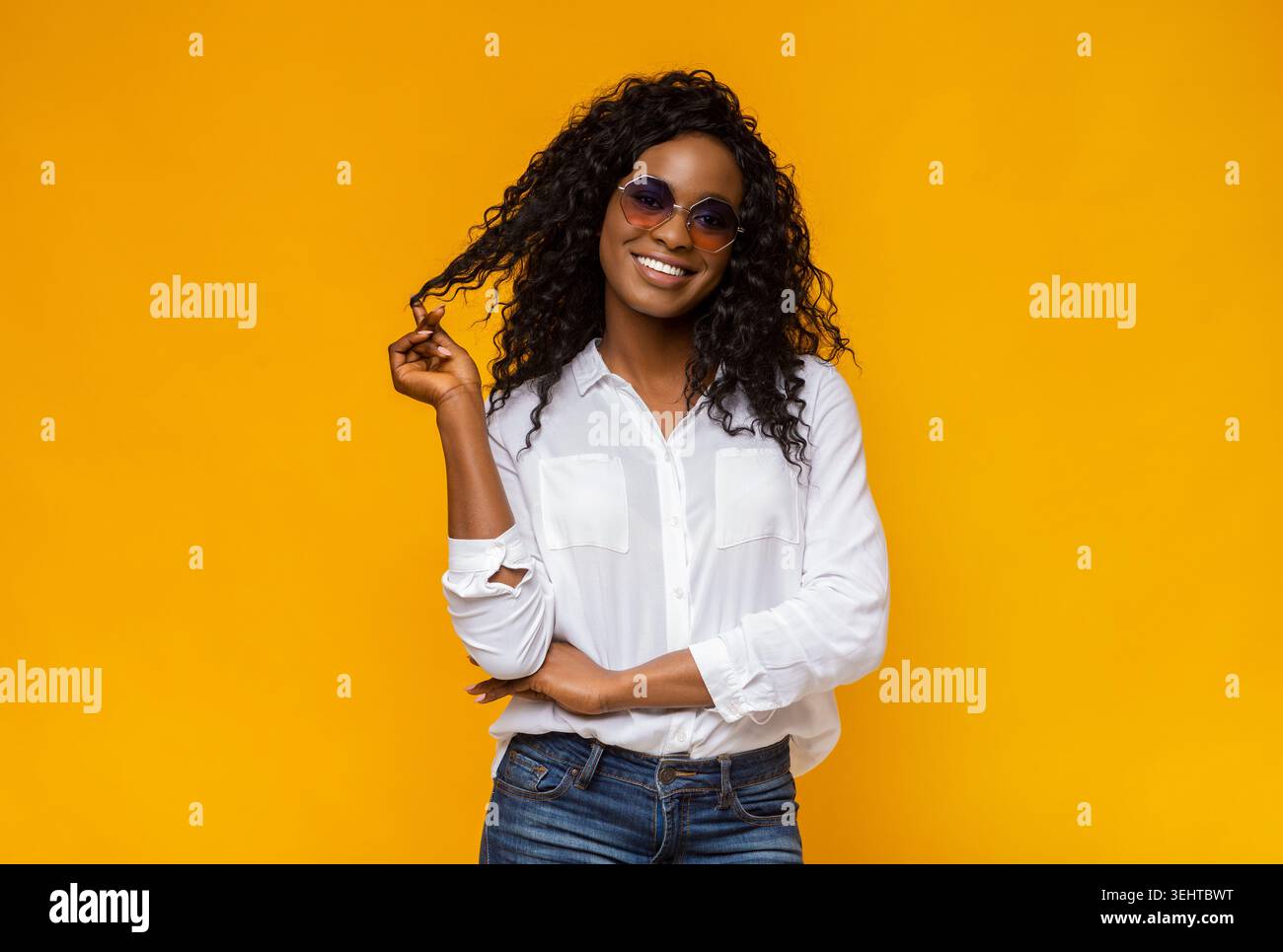 Young Woman in Sunglasses Poses Confidently Against a Vibrant Yellow Background Stock Photo