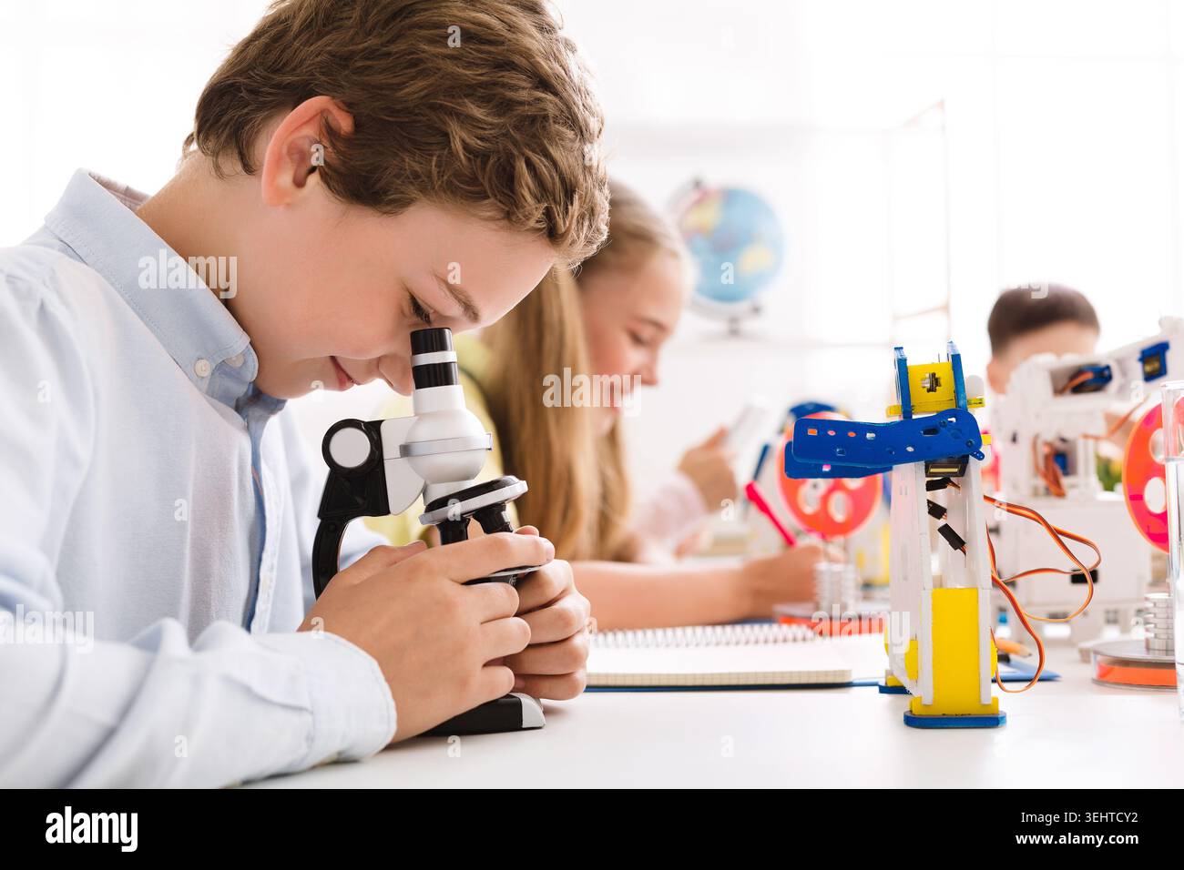 Students Engaged in Hands On Learning With Microscopes and Robotics in a Bright Classroom Stock Photo