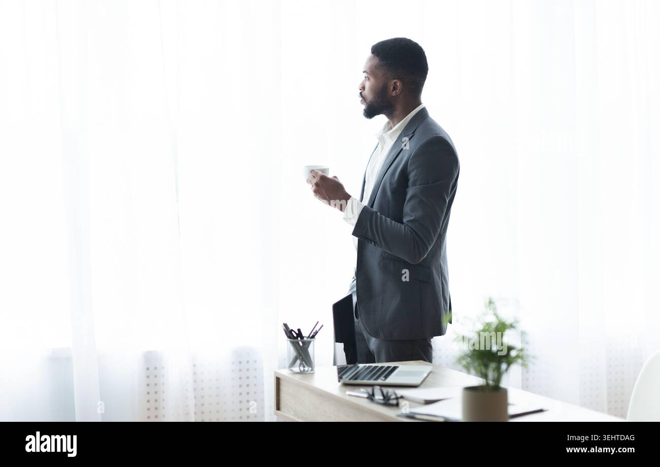 Thoughtful black businessman looking out of window and drinking coffee Stock Photo