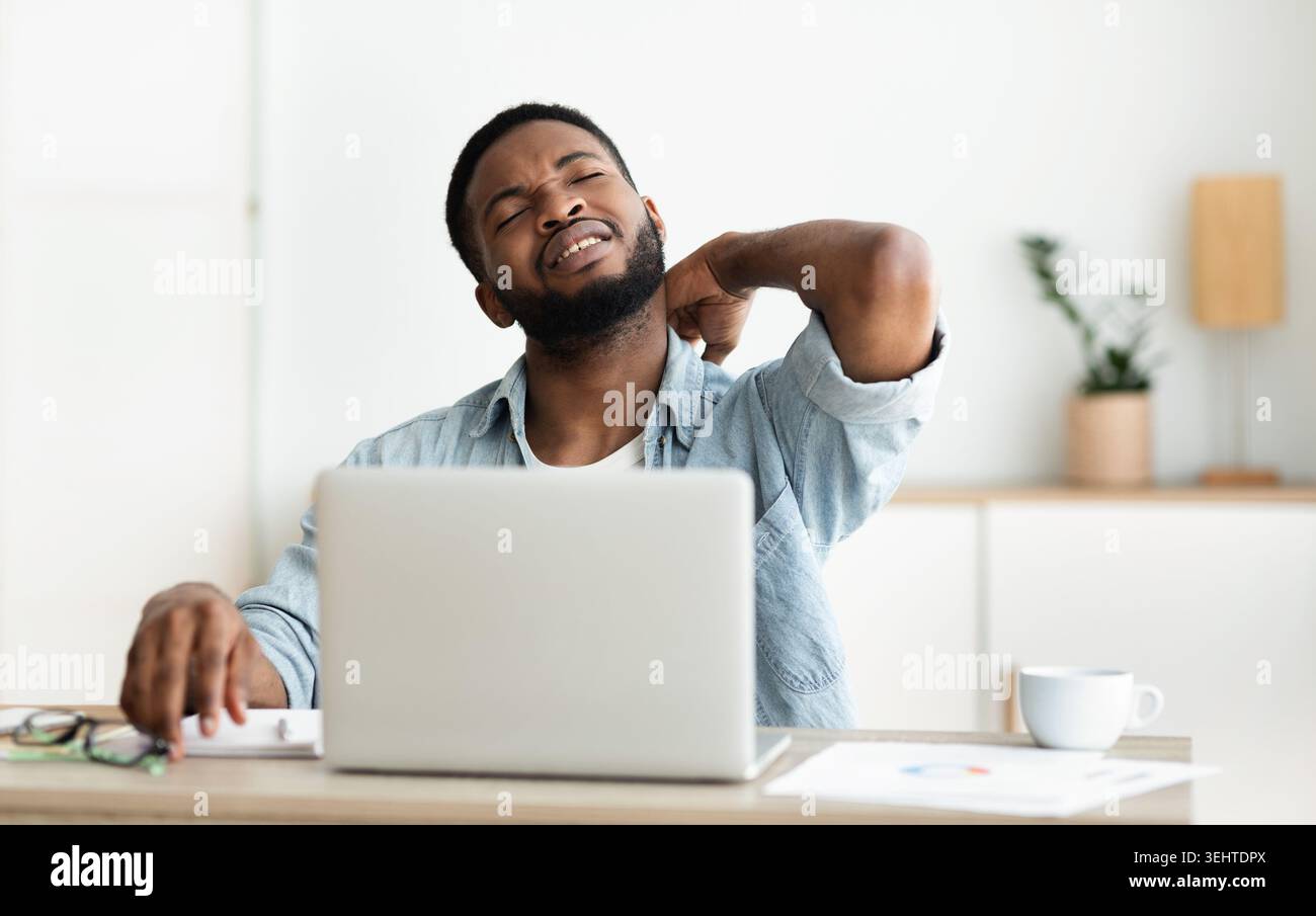 Black man suffering from neck pain while working on laptop Stock Photo