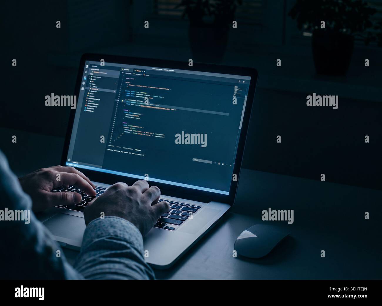 Person works on computer in dark room while writing code for web application or software project Stock Photo