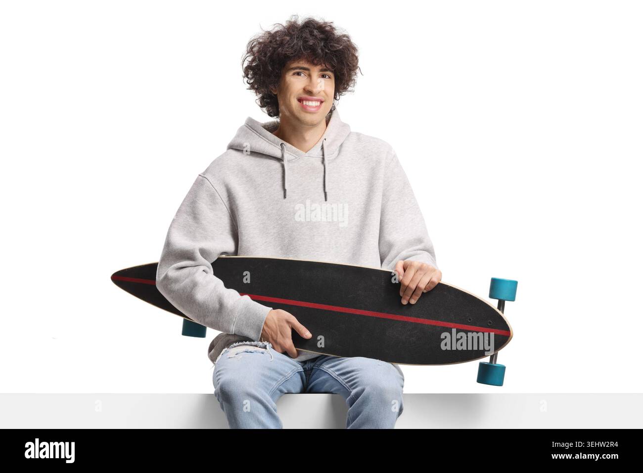 Guy holding a longboard and sitting on a panel isolated on white background Stock Photo