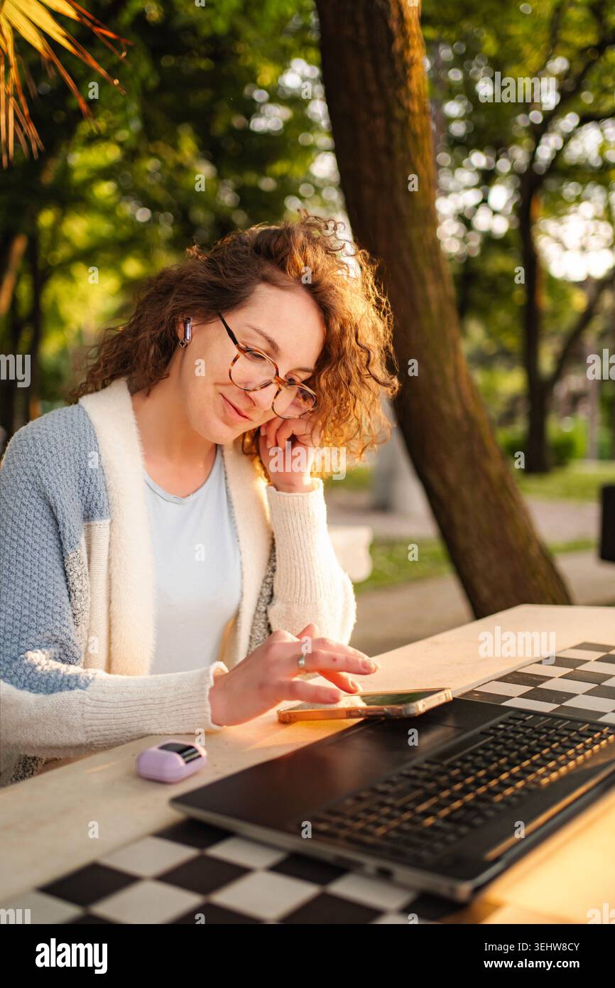 Woman working remotely outdoors using laptop and smartphone Stock Photo