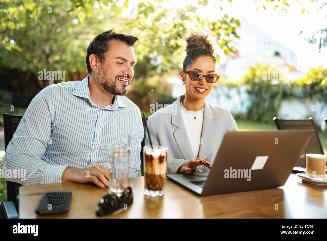 Business colleagues collaborating on laptop at outdoor cafe Stock Photo