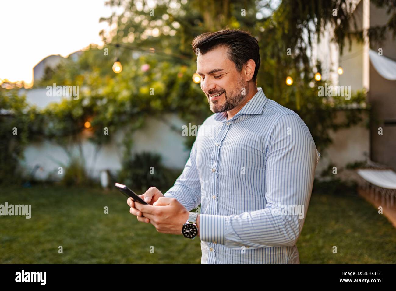 Smiling man networking using smartphone in backyard garden Stock Photo