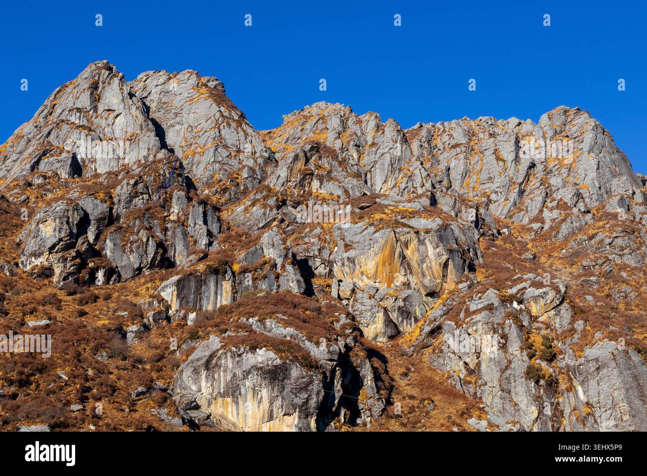 Rugged rocky mountain cliffs with dry golden grass under a clear blue sky. Stock Photo