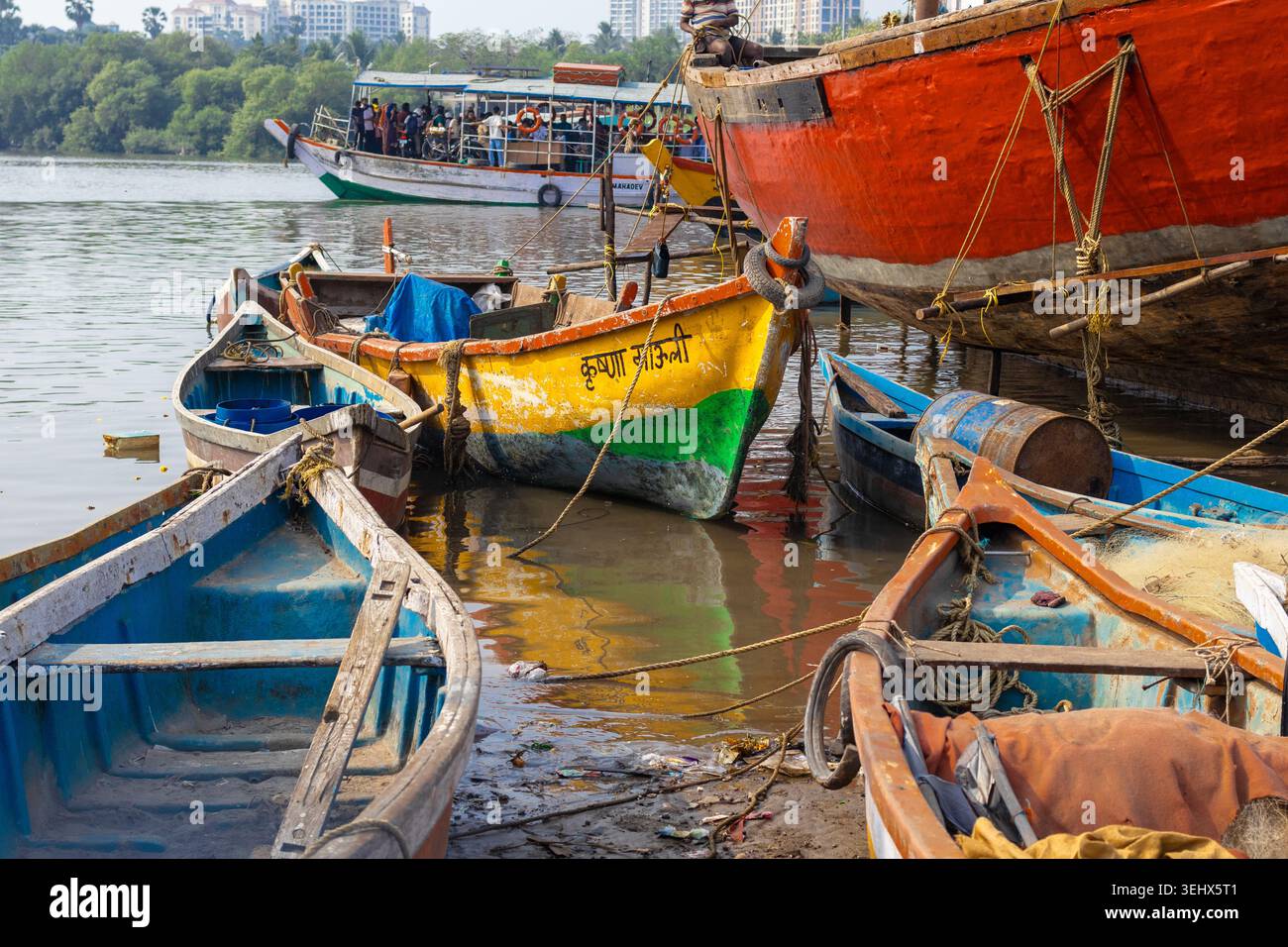 Traditional wooden fishing boats moored on a muddy shore with a crowded passenger ferry boat operating in the background, Mumbai, India Stock Photo