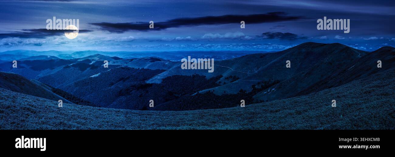 beautiful panorama of mountainous landscape at night. full moon over wide view of cloudy sky over the grassy slope of a mountain ridge. mysterious sum Stock Photo