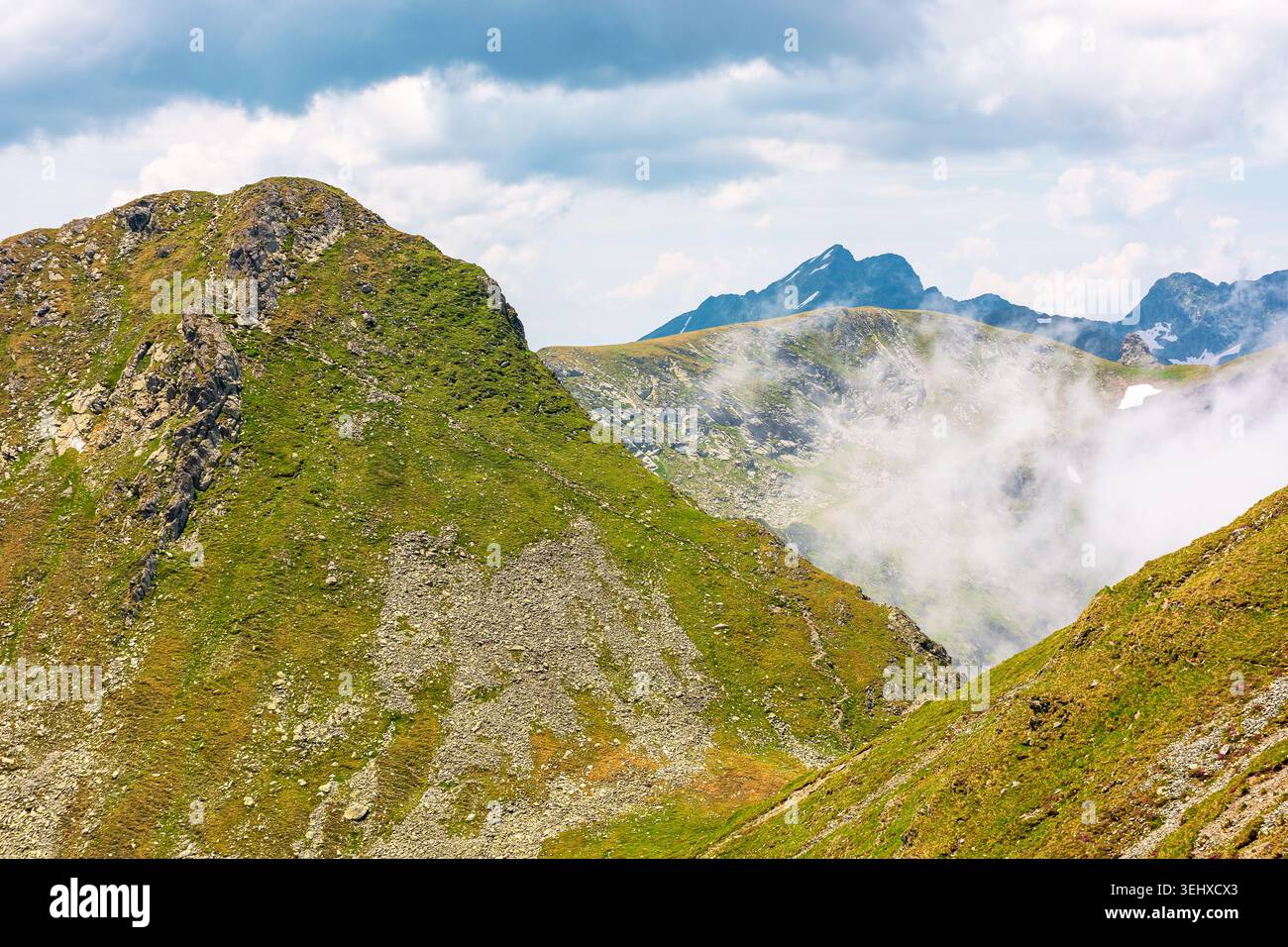 mountain landscape with steep rocky slopes. romania travel background. clouds on a blue sky above fagaras mountain ridge. stunning weather in summer Stock Photo