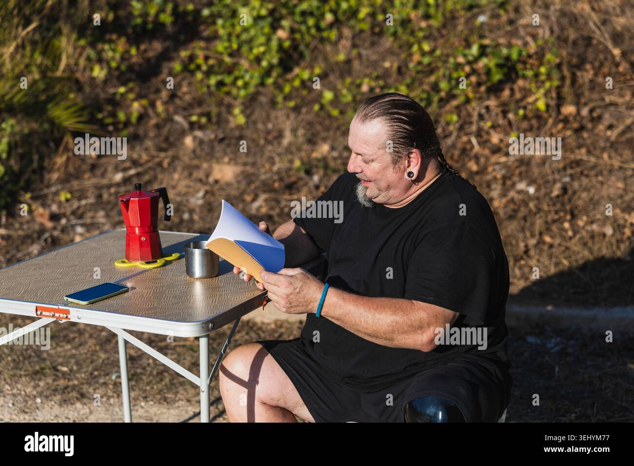 Man with prosthetic leg reading outdoors drinking coffee Stock Photo