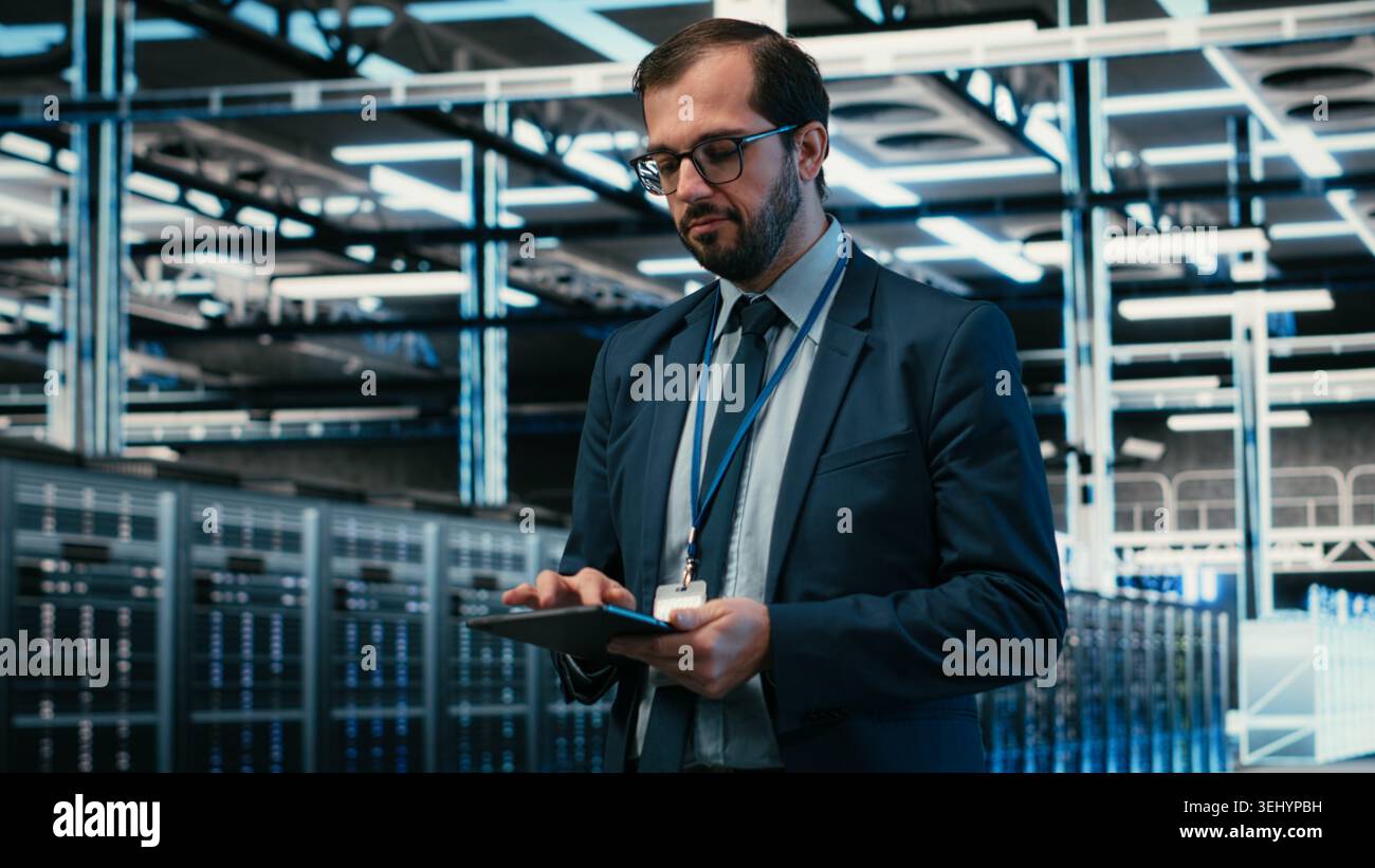Data center computer scientist using tablet app, managing equipment powering online platforms. Man walks in server room, doing maintenance on digital storage systems using touchscreen device, camera B Stock Photo