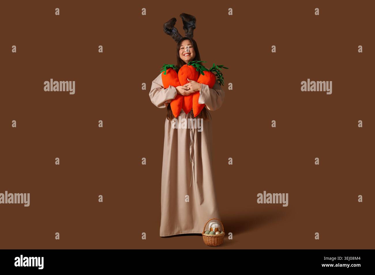 Young happy woman in Easter bunny ears holding plush carrots near ...