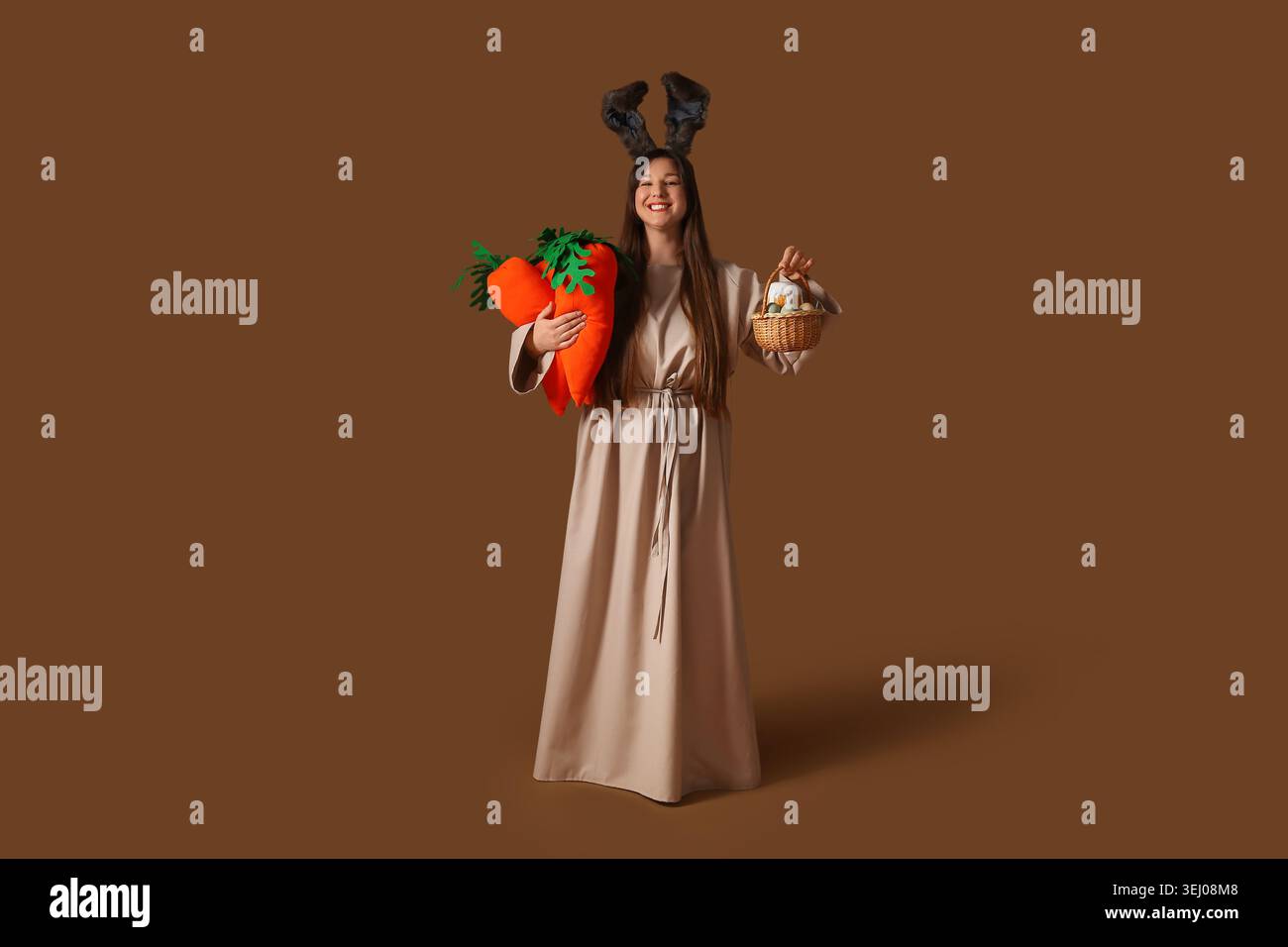 Young happy woman in Easter bunny ears holding plush carrots and basket ...