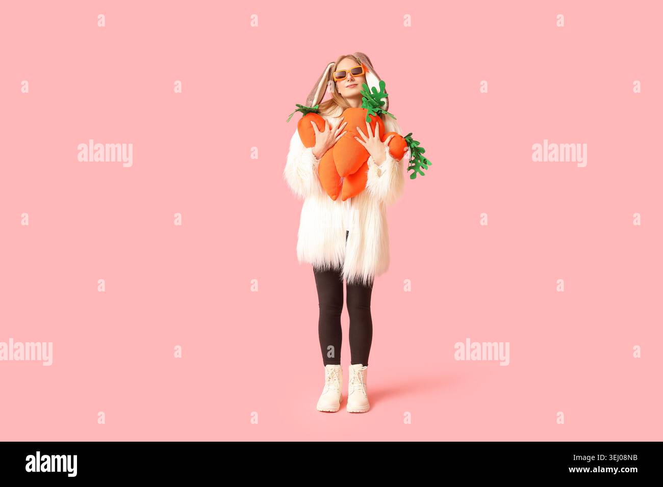 Beautiful woman in bunny ears with toy carrots on pink background ...
