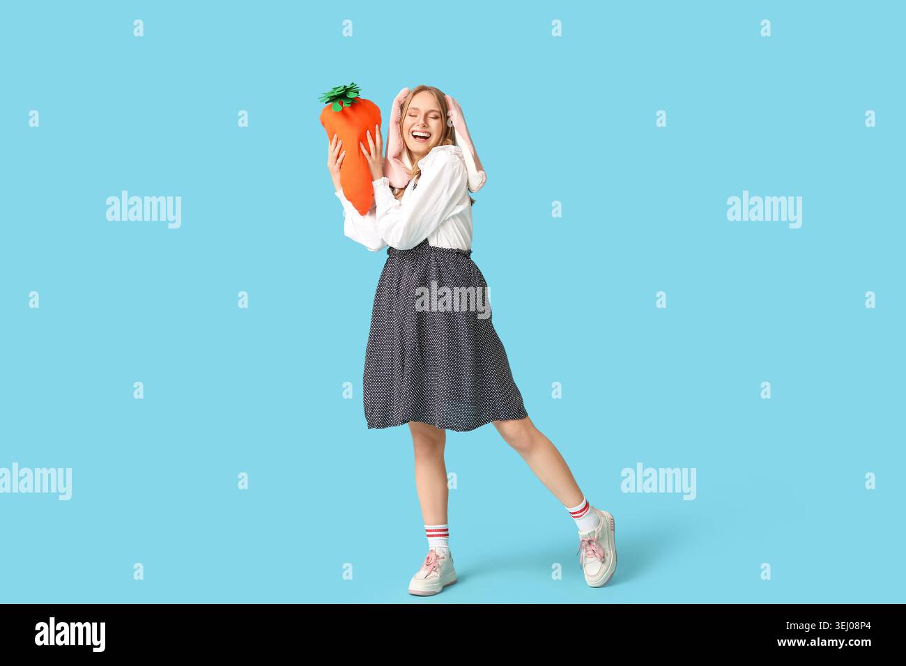 Happy woman in bunny ears with toy carrot on blue background. Easter ...