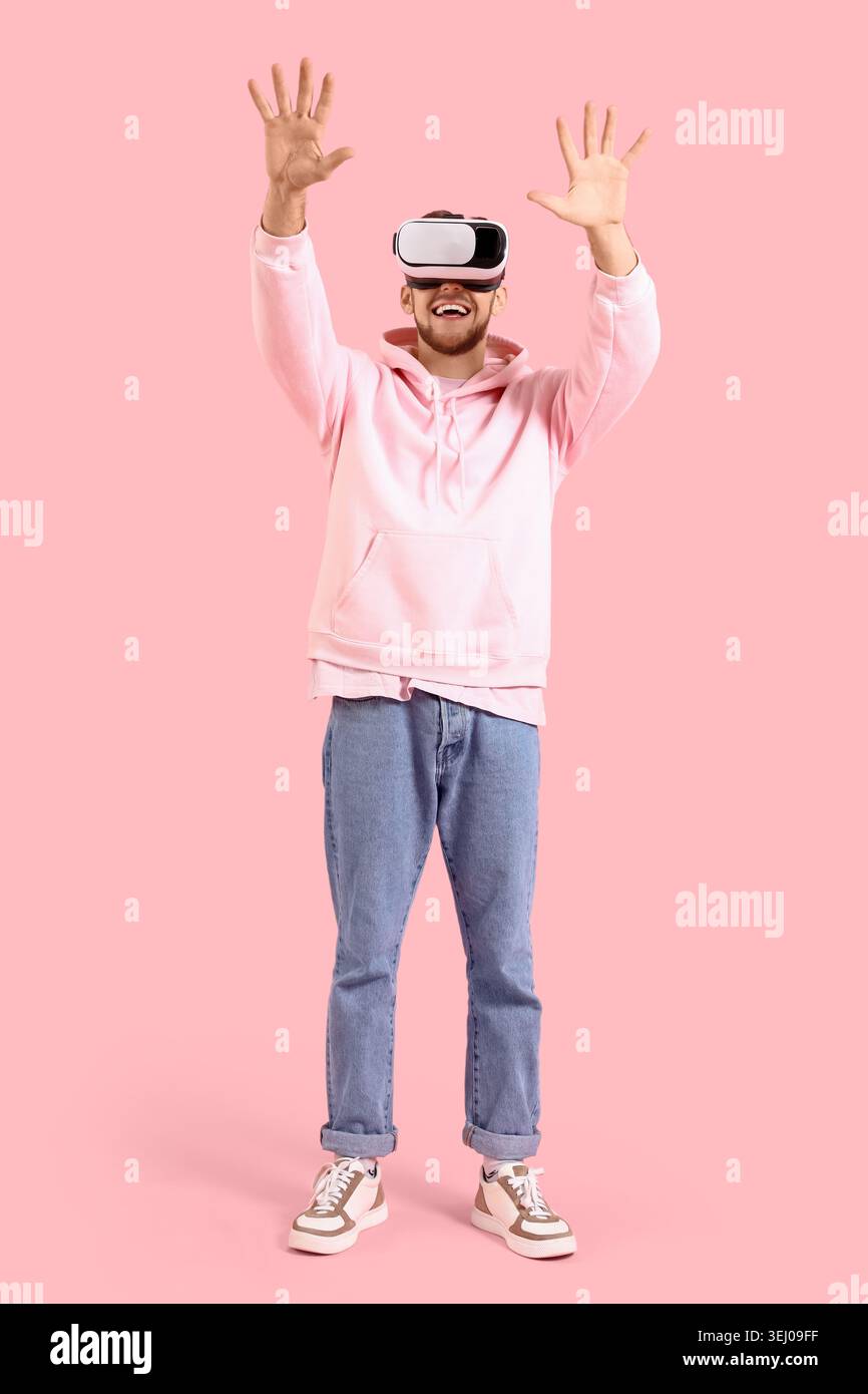 Young bearded man using VR glasses on pink background Stock Photo