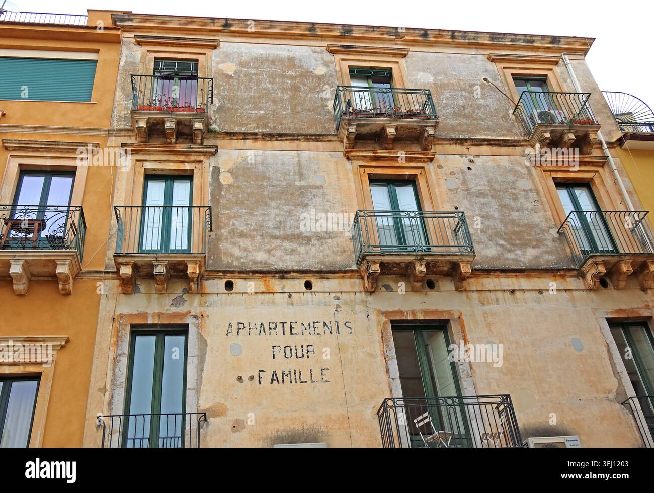 Sicily family apartments exterior in Sicily, Italy, with traditional balconies and faded stone facade. Stock Photo