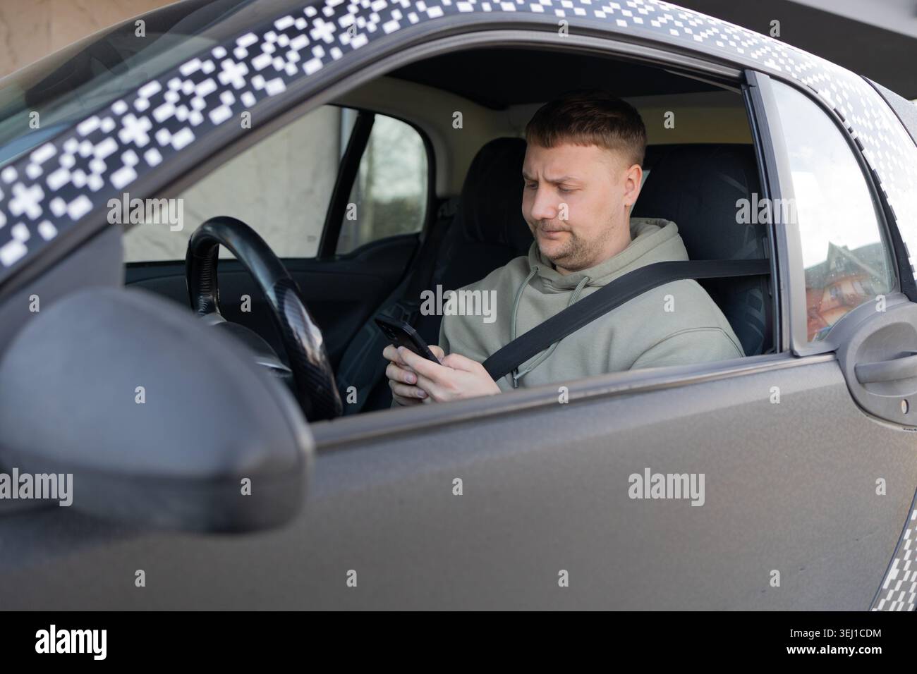 Driver using smartphone while wearing seatbelt in parked car Stock Photo