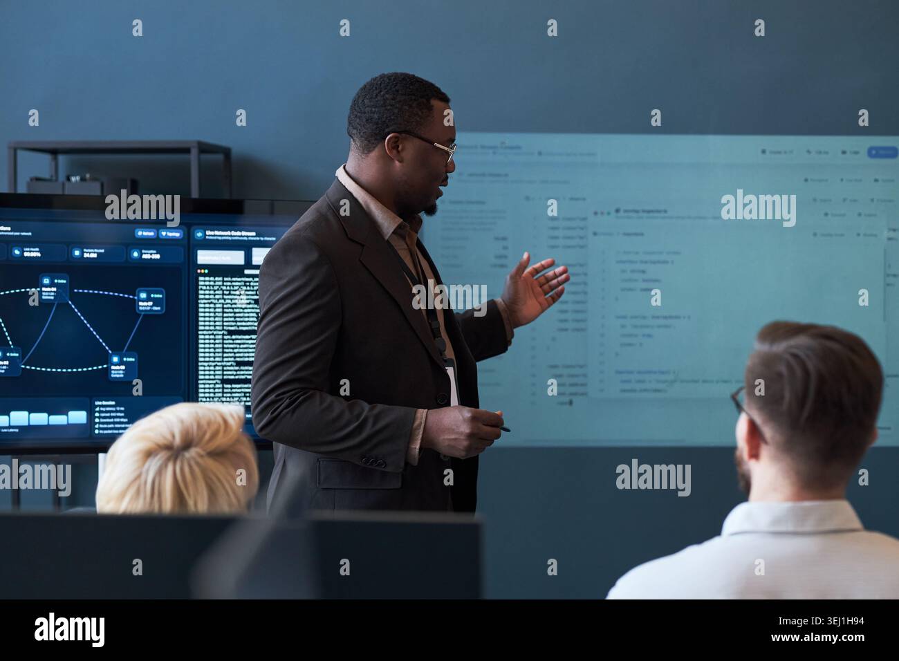 Medium shot of Black middle aged businessman presenting software dashboard to colleagues during office meeting, explaining data workflow. Ideal for business training, teamwork, IT strategy Stock Photo
