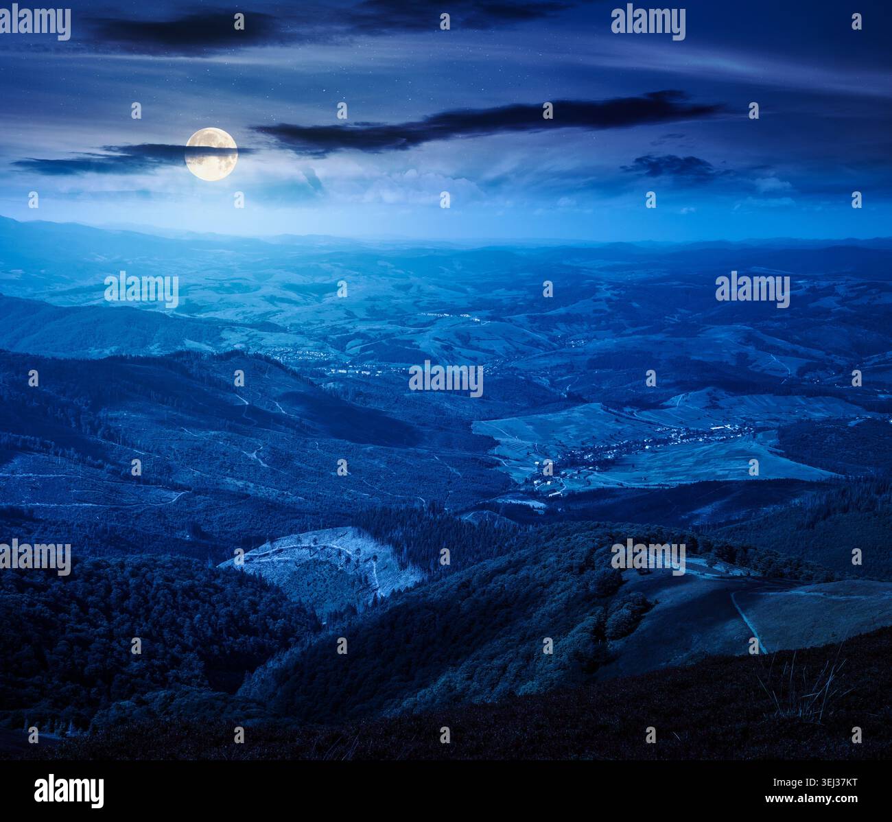 mountainous countryside scenery at night. view of cloudy sky above the valley. full moon over colorful meadows and trees on hill in dappled light. mys Stock Photo