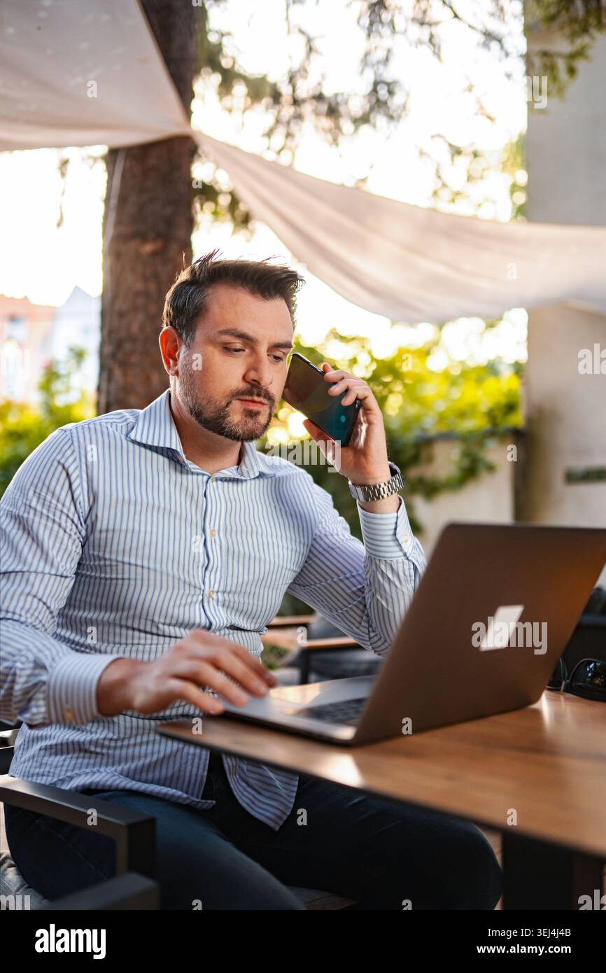 Man working remotely outdoors using laptop and smartphone Stock Photo
