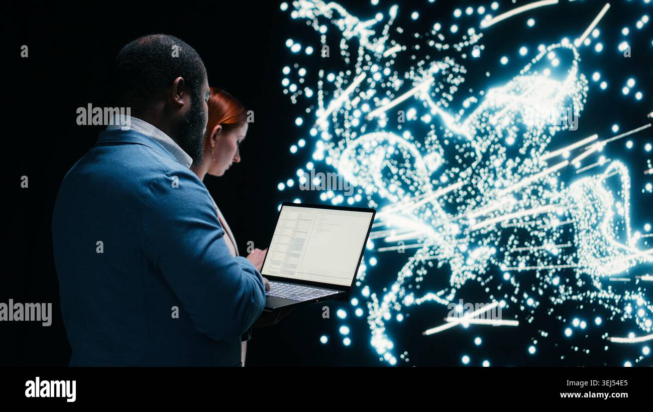 Team of AI startup data scientists implement deep learning algorithms with laptop, collaborating. Coworkers coding, modifying artificial intelligence neural network architecture with device, camera B Stock Photo