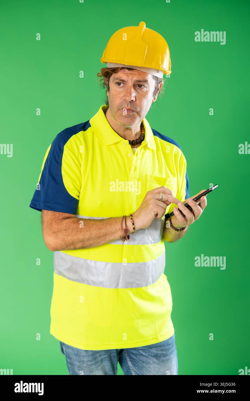 Man wearing in reflective polo and hard hat scrolls phone screen Stock Photo