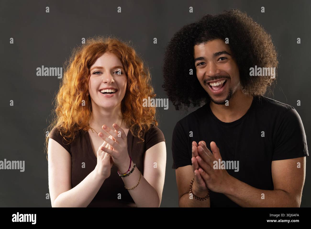 Cheerful multiracial couple clapping their hands, celebrating with big smiles Stock Photo