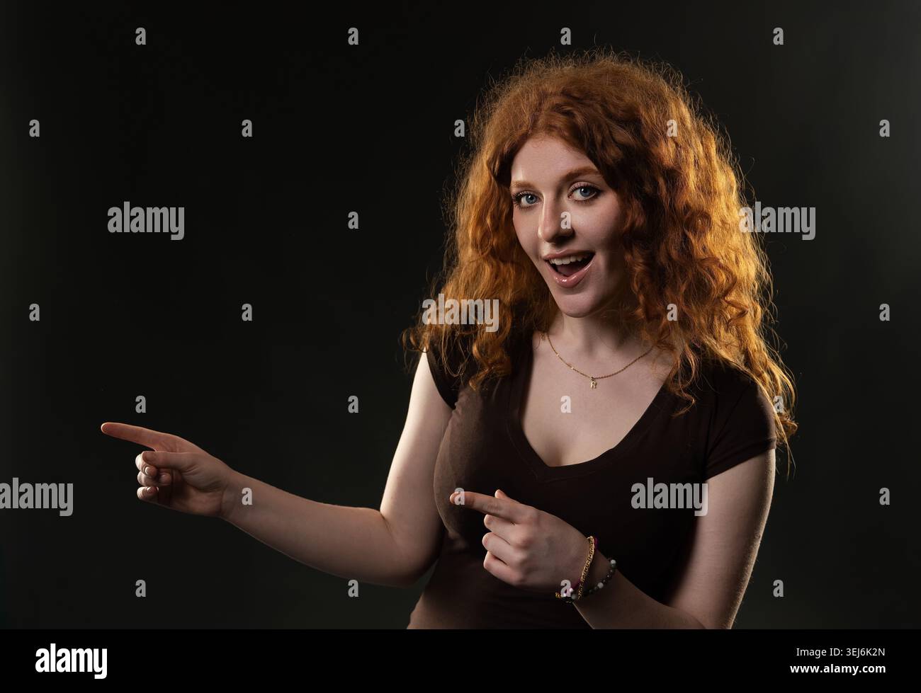 Redhead woman pointing left and down expressing surprise or excitement Stock Photo