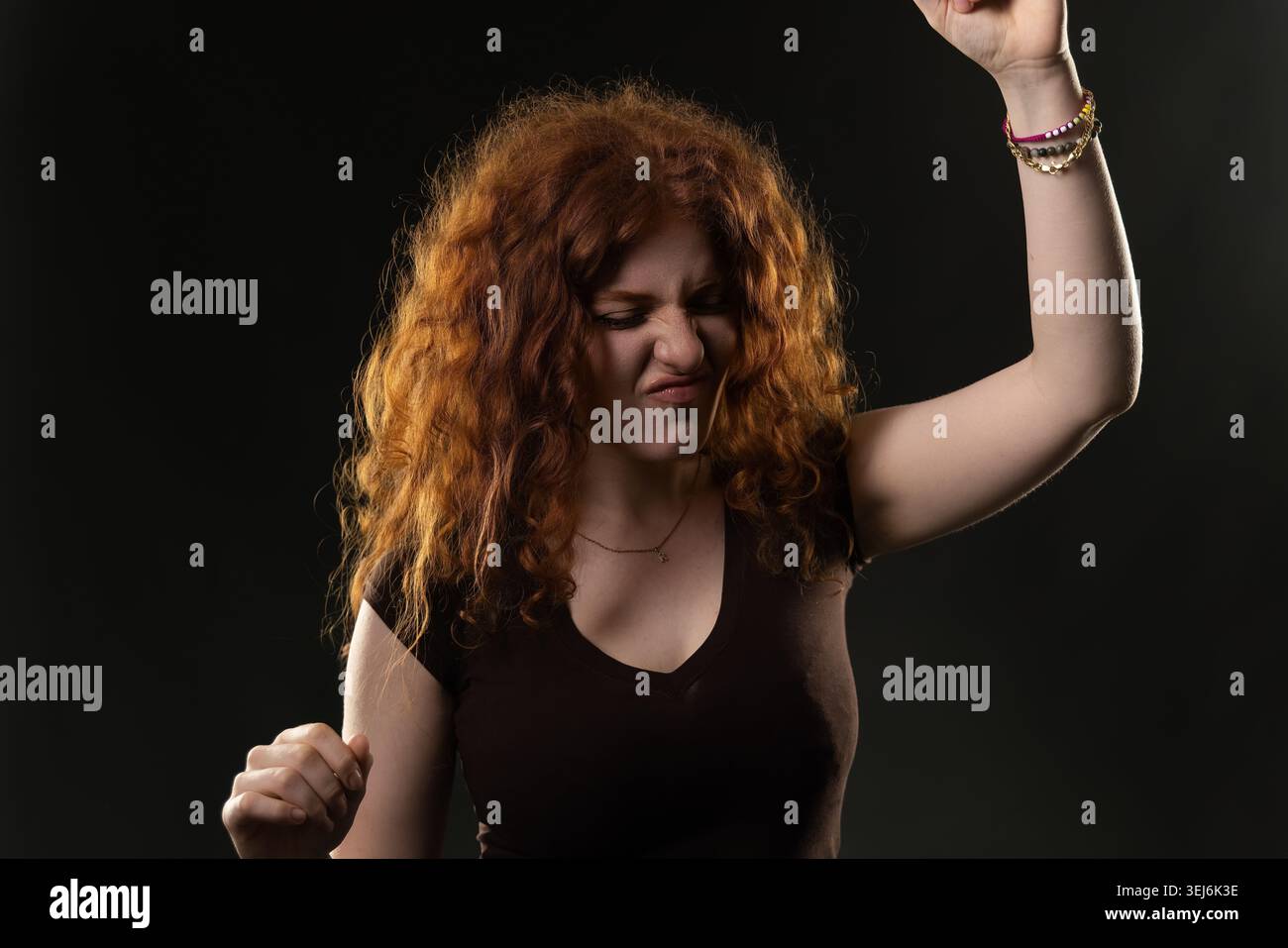 Young woman with curly red hair dancing actively, expressing strong emotion Stock Photo