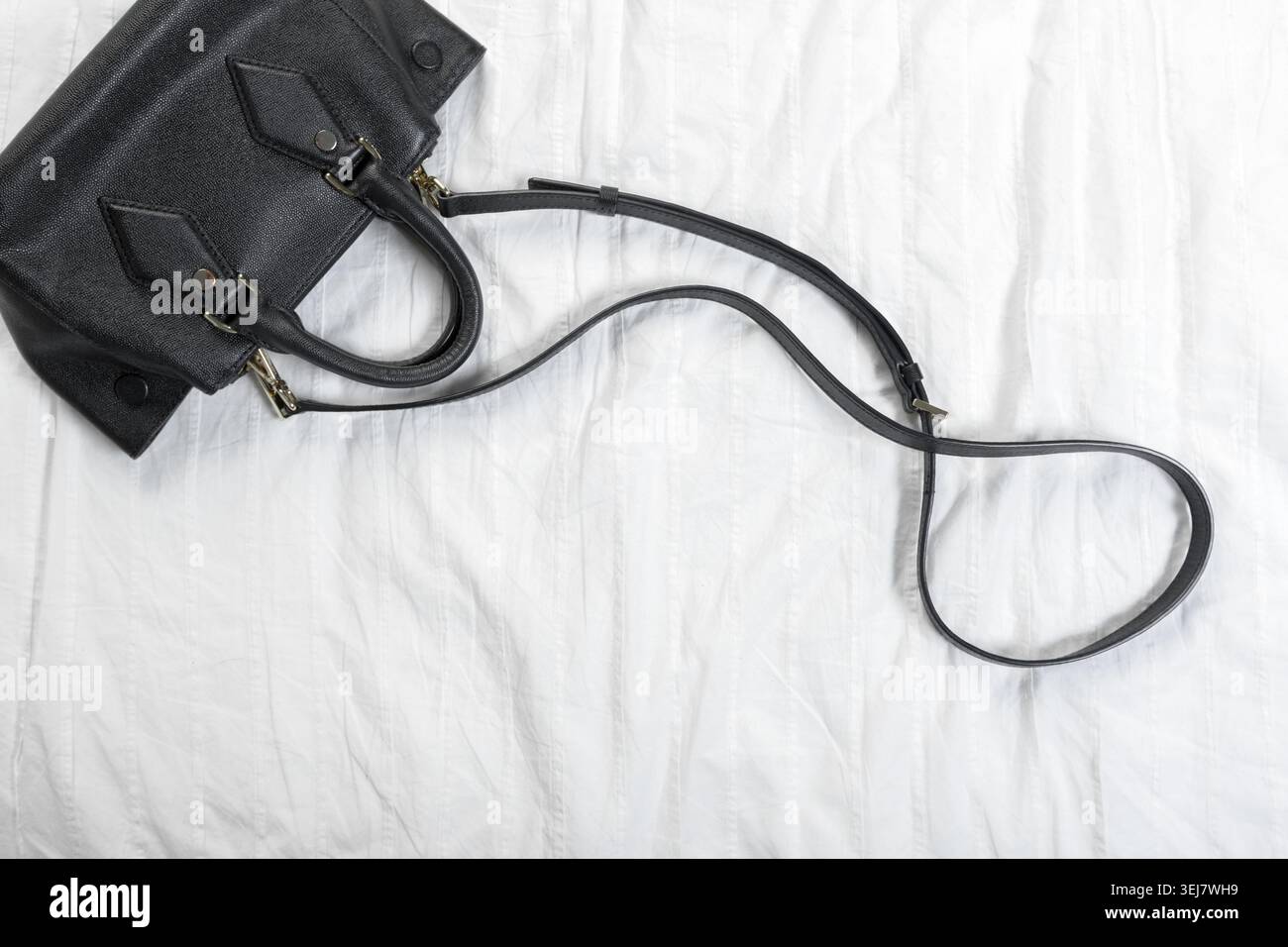 Black handbag placed on a soft white surface in a simple indoor setting Stock Photo