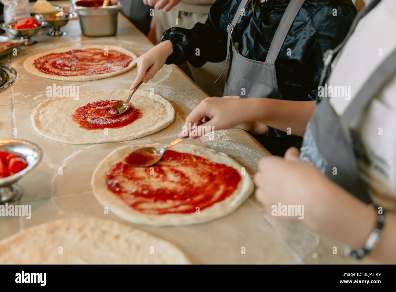 Chef preparing fresh pizzas in restaurant kitchen with tomato sauce Stock Photo