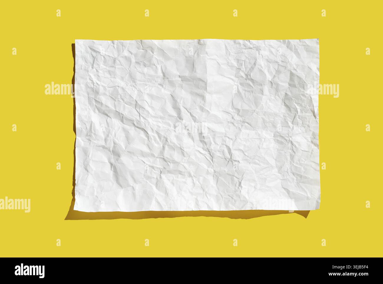 Crumpled white paper sheet on bright yellow background highlighting texture and shadows Stock Photo