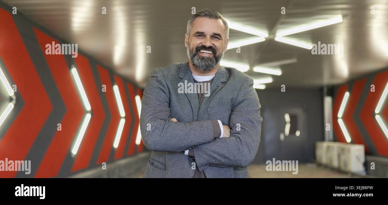 A gray-haired fifty-year-old man businessman in an underground parking lot stands with his arms folded across his chest Stock Photo