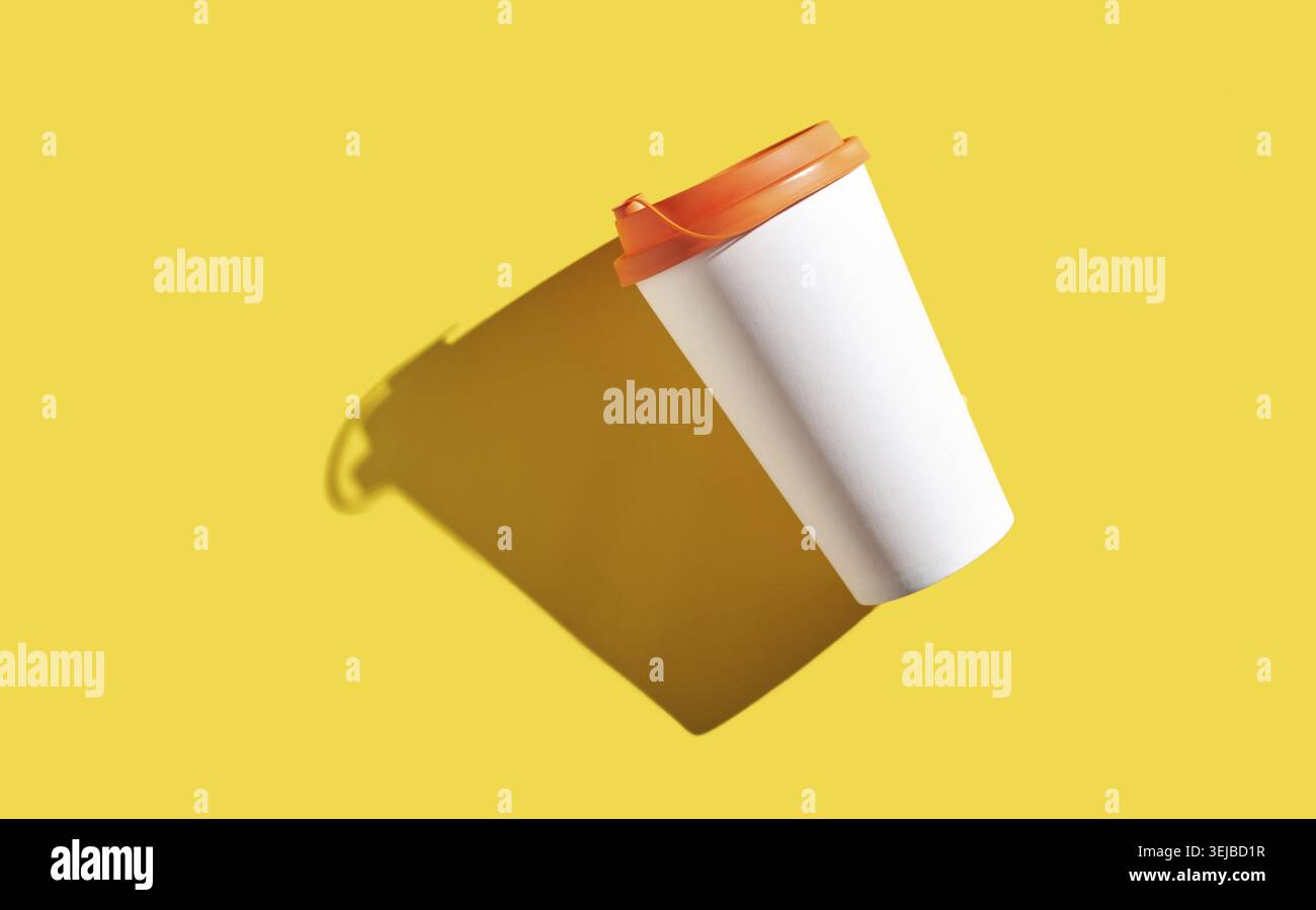 Floating white coffee cup with orange lid on yellow background casting shadow Stock Photo
